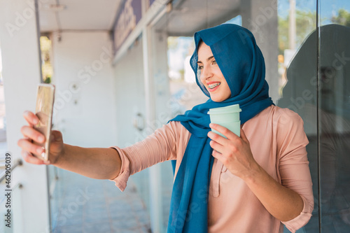 Smiling Muslim woman taking selfie in city