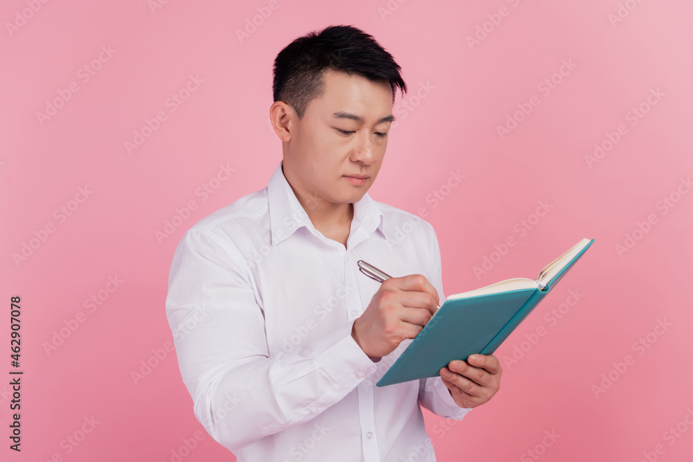 Profile side photo of young asian man write notes plan to-do list isolated over pink color background