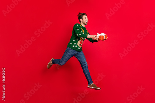 Full size profile side photo of smiling crazy running man give christmas present celebration isolated on red color background