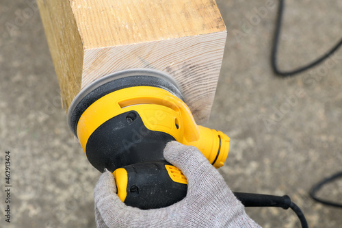 .Eccentric orbital sander, grinder machine for wood with a worker's hand on wooden surface, close up