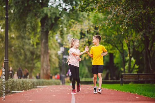 Sports and fitness in adolescence. Caucasian twins boy and girl run on the jogging track in the city park. Two children brother and sister for 10 years running on a rubberized outdoor treadmill © Elizaveta