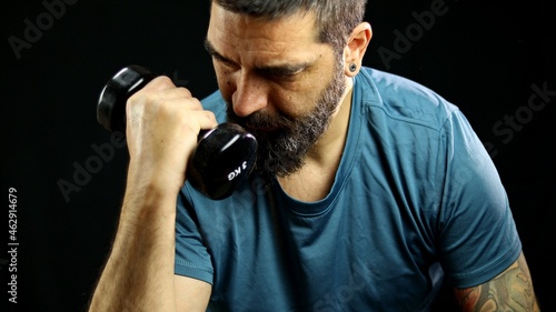 Man in sportswear doing biceps curls with 3kg dumbbells, workout on black background. Man doing biceps exercise sitting.