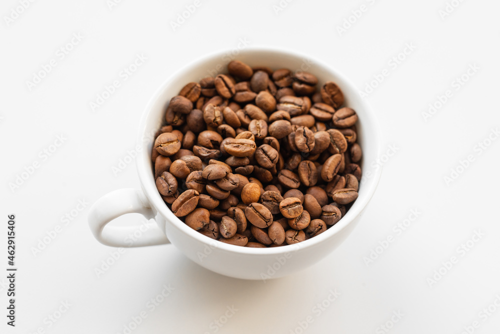 A white cup filled with brown coffee beans on white background