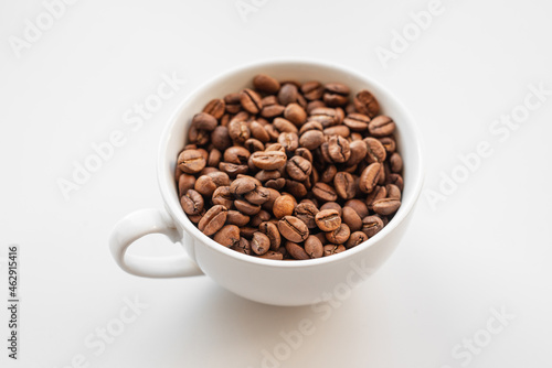 A white cup filled with brown coffee beans on white background