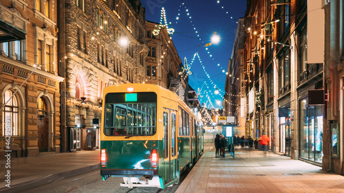 Helsinki, Finland. Tram Departs From Stop On Aleksanterinkatu Street. Night Evening Christmas Xmas New Year Festive Illumination On Street. Beautiful Street Decorations During Winter Holidays