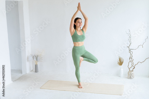 Happy young woman in green sportswear practices yoga in Tree pose. Home yoga.