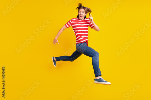 Photo of pretty sweet young guy dressed red t-shirt running jumping modern gadget smiling isolated yellow color background