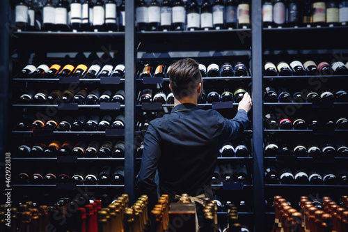 Sommelier Bartender man at wine shop full of bottles with alcohol drinks, back view photo