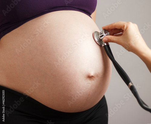 pregnant woman being examined by doctor on gray studio background, stethoscope on belly,health care concept