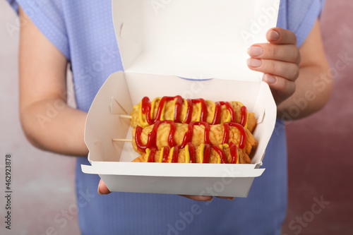 Photography Woman holding box of delicious corn dogs with mustard and ketchup on pink backgr