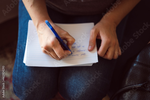 Close up shot of female's hand writing down a message on the notepad in her lap