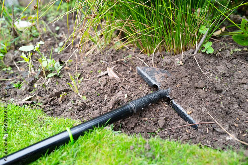 Steel half moon edger and spade seen in worked flowerbed soil.