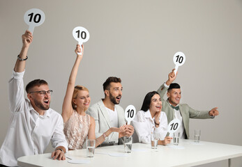 Panel of judges holding signs with highest score at table on beige background