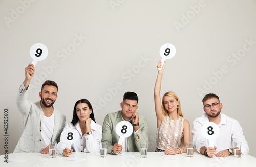 Panel of judges holding different score signs at table on beige background photo