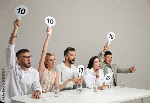 Panel of judges holding signs with highest score at table on beige background photo