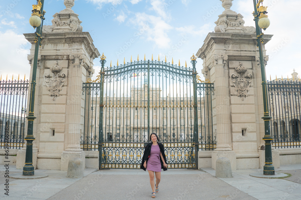 urban lifestyle outdoors portrait of young happy and beautiful Asian Chinese woman in sweet Autumn dress enjoying Madrid city tour relaxed and cheerful at palace iron gate
