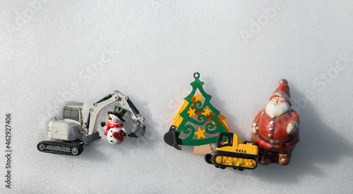 two models of toy excavators, souvenir snowman, figurine of Santa Claus, Christmas tree made of wood lie on white snow