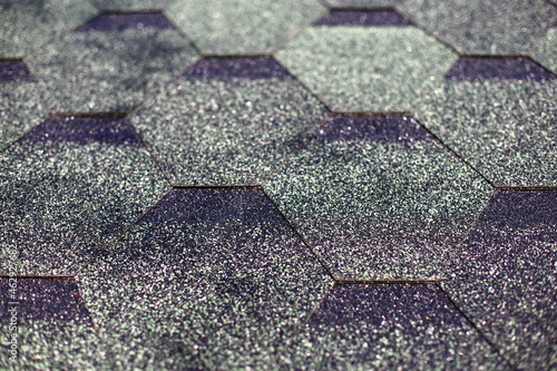 Waterproof hexagonal green black shingle closeup sprinkled with strong fines basalt stone chips firmly adhered to bitumen base. Modern affordable popular reliable roofing