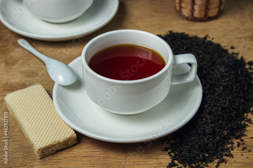 A cup of tea next to black loose tea. Cup of strong black tea on wooden background