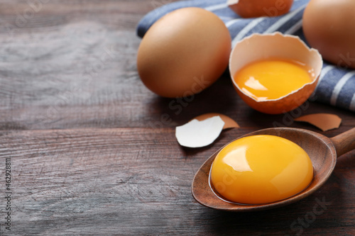 Spoon with raw egg yolk on wooden table, closeup. Space for text photo
