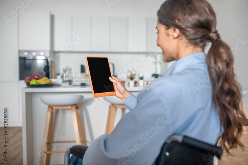 A young cute girl sitting in the kitchen with a smartphone in hands