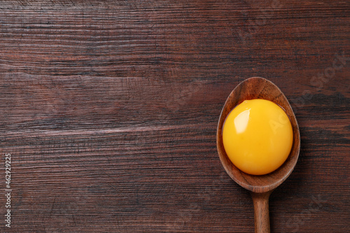 Spoon with raw egg yolk on wooden table, top view. Space for text photo