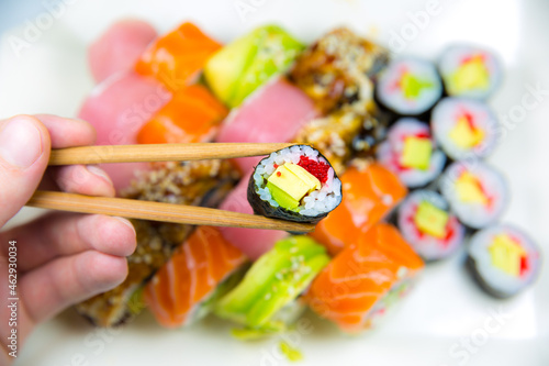 Man takes Tasty Colorful assorted Set of different type Sushi with chopsticks. Dinner in Japanese style. Healthy food. Filadelfia and Maki sushi rolls with Avocado, Tuna, Salmon, fish and Prawns.