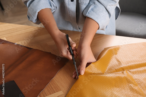 Woman cutting orange leather with scissors at wooden table  closeup