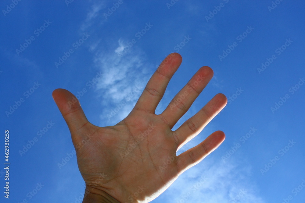 Hand palm of young caucasian man on background blue clear sky with white cirrus cloud sunny summer day close-up. Symbolizes person that reaching dream as high sky Hand palm of young caucasian man on background blue clear sky with white cirrus cloud sunny summer day close-up. Symbolizes person that reaching dream as high sky