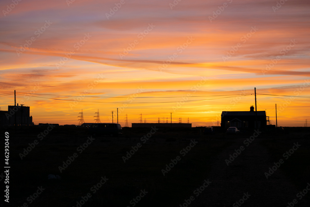 Colorful sunset over silhouettes of houses and power columnts at Dungeness, Kent, England