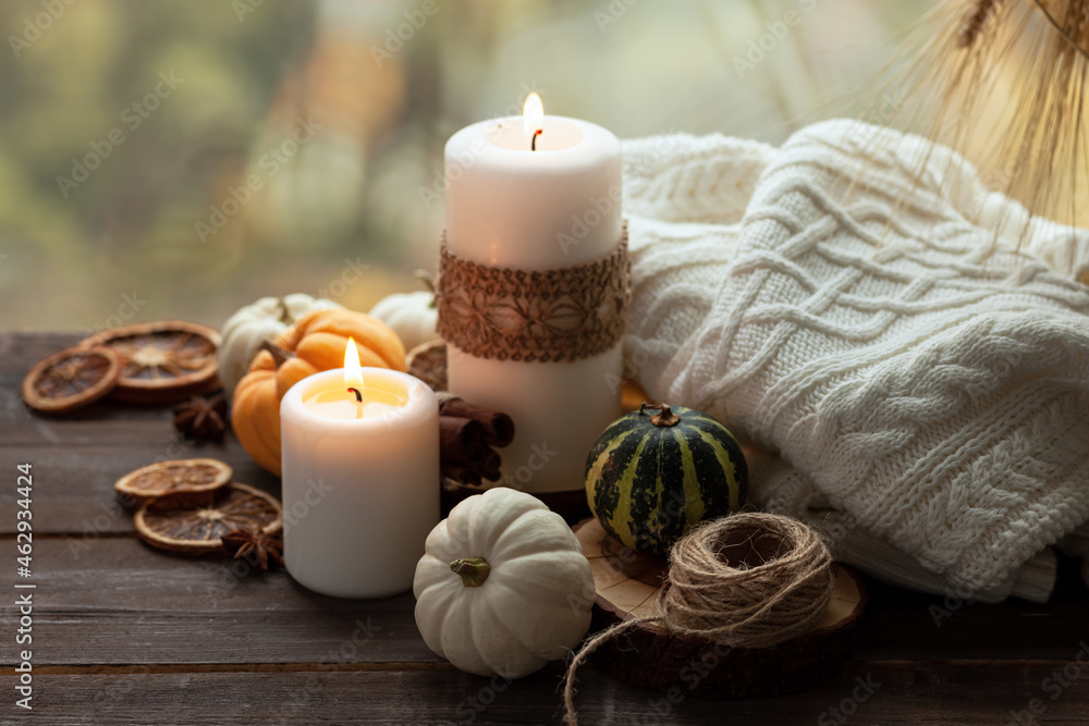 Autumn composition with candles, mini munchkin pumpkins, warm wool knitted plaid on the wooden wind sill. Dark colors, low key. Cozy home atmosphere, Thanksgiving decor, fall colors. Close up