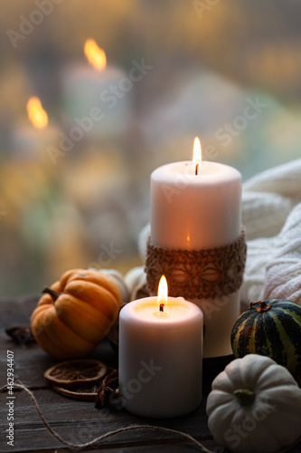 Autumn composition with candles, mini munchkin pumpkins, warm wool knitted plaid on the wooden wind sill. Dark colors, low key. Cozy home atmosphere, Thanksgiving decor, fall colors. Close up