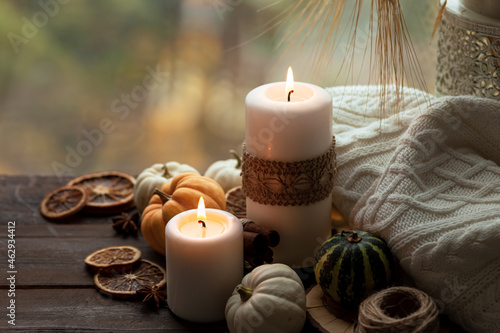 Autumn composition with candles  mini munchkin pumpkins  warm wool knitted plaid on the wooden wind sill. Dark colors  low key. Cozy home atmosphere  Thanksgiving decor  fall colors. Close up