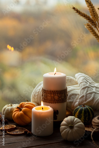 Autumn composition with candles, mini munchkin pumpkins, warm wool knitted plaid on the wooden wind sill. Dark colors, low key. Cozy home atmosphere, Thanksgiving decor, fall colors. Close up