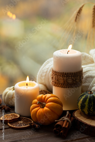 Autumn composition with candles  mini munchkin pumpkins  warm wool knitted plaid on the wooden wind sill. Dark colors  low key. Cozy home atmosphere  Thanksgiving decor  fall colors. Close up