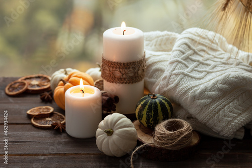 Autumn composition with candles  mini munchkin pumpkins  warm wool knitted plaid on the wooden wind sill. Dark colors  low key. Cozy home atmosphere  Thanksgiving decor  fall colors. Close up