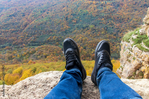 A man admiring the scenic views, sitting on the edge of a cliff, against the backdrop of a stunning landscape
