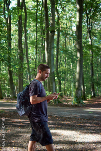 A Hispanic man with a backpack using the phone while walking in the forest