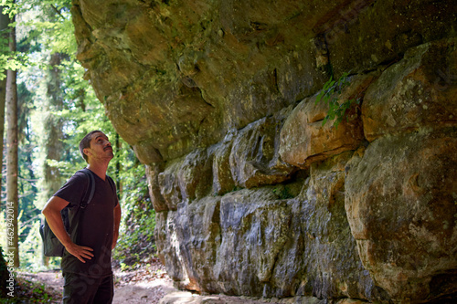 An adult Hispanic hiker with a backpack looking at cave walls in a forest