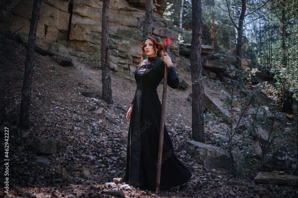 klik Allerede mikrofon Evil witch with a staff in the forest. Slavic witch creates red magic. A  young woman in a black dress and a crown embroidered with beads. Stock-foto  | Adobe Stock