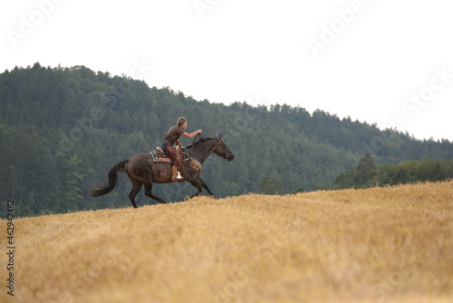 countrygirl. Frau galoppiert mit schwarzem Pferd über ein Stoppelfeld photo