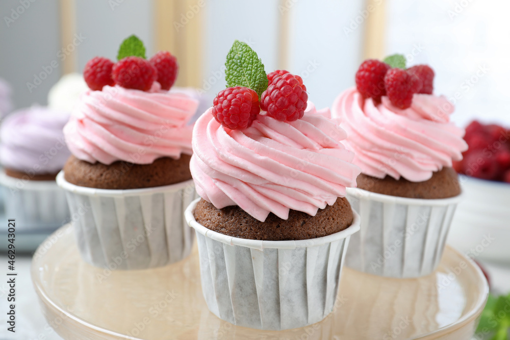 Delicious cupcakes with cream and raspberries on stand, closeup Delicious cupcakes with cream and raspberries on stand, closeup