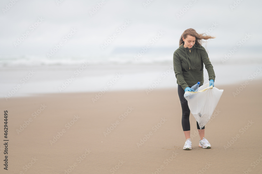 Sand beach. Girl volunteer in gloves collects trash in a bag. The concept is to protect wildlife from poisons and toxins. Environmental and social issues. There is an empty space for insertion. Sand beach. Girl volunteer in gloves collects trash in a bag. The concept is to protect wildlife from poisons and toxins. Environmental and social issues. There is an empty space for insertion.