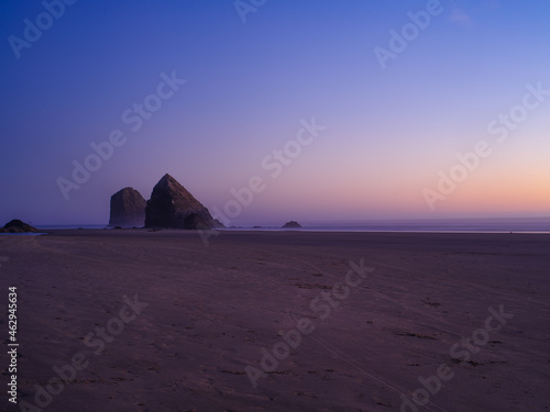 A beautiful landscape - a sandy ocean shore  two rocks can be seen in the distance. Dust. Clear blue cloudless sky. Calm scenes. Beauty of nature. Advertising of tourist destinations.