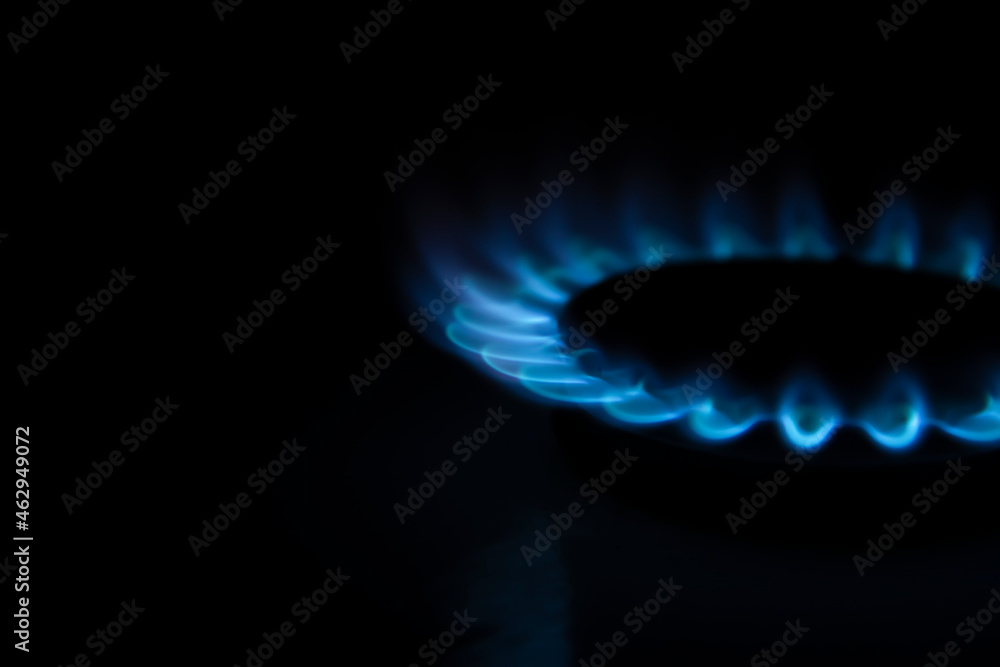 Side view of burning gas stove with blue flame in dark kitchen. Black background. Copy space for your text. Selective focus. Biogas or natural gas. Fuel industry theme. Side view of burning gas stove with blue flame in dark kitchen. Black background. Copy space for your text. Selective focus. Biogas or natural gas. Fuel industry theme.