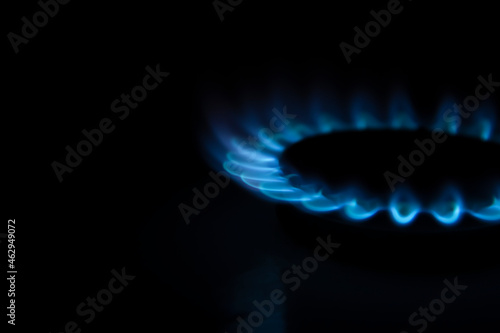 Side view of burning gas stove with blue flame in dark kitchen. Black background. Copy space for your text. Selective focus. Biogas or natural gas. Fuel industry theme.