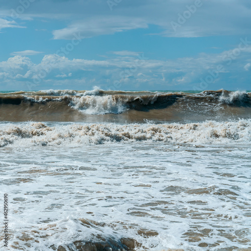 big sea wave runs along the beach against the blue cloudy sky