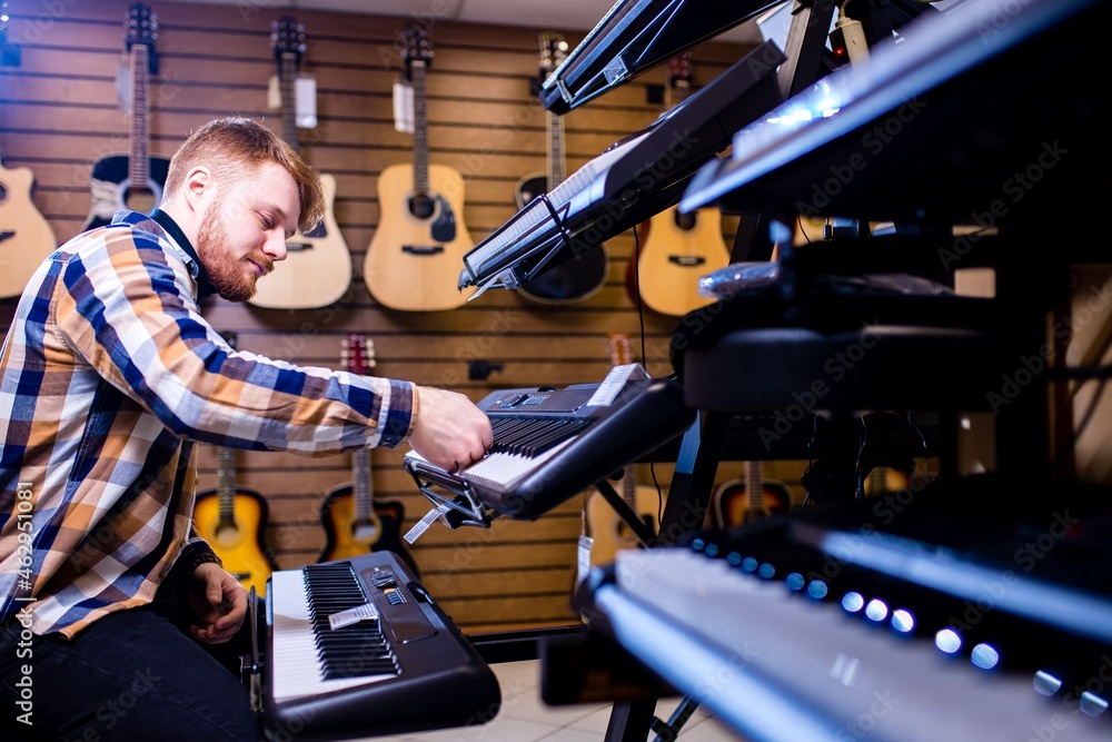redhair ginger beard man is playing on piano in music store