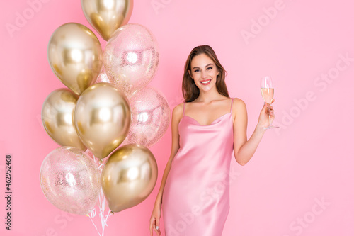 Smiling young woman holds glass of champagne stands near air balloons. came to party. Celebration 