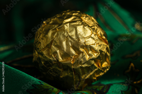 Tasty Chocolate Praline Wrapped with Golden Foil on Gorgeous Green Backdrop